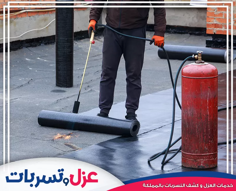 الصورة تُظهر فنيًا يطبق لفائف عزل (رولات بتومينية)، وهي جزء من خدمات شركة عزل اسطح بالطائف لضمان.